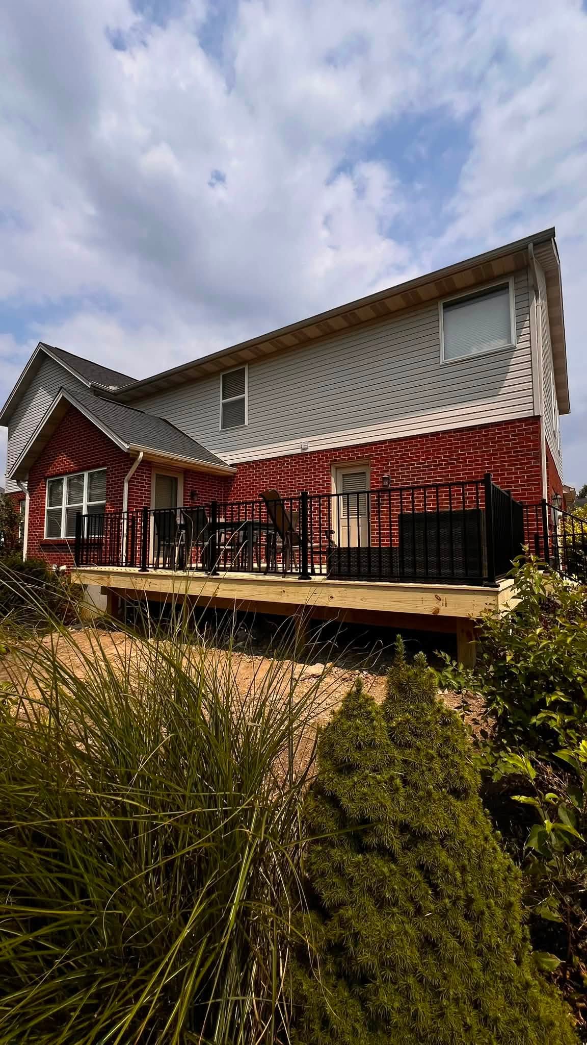Composite deck with black aluminum railing behind a red brick home