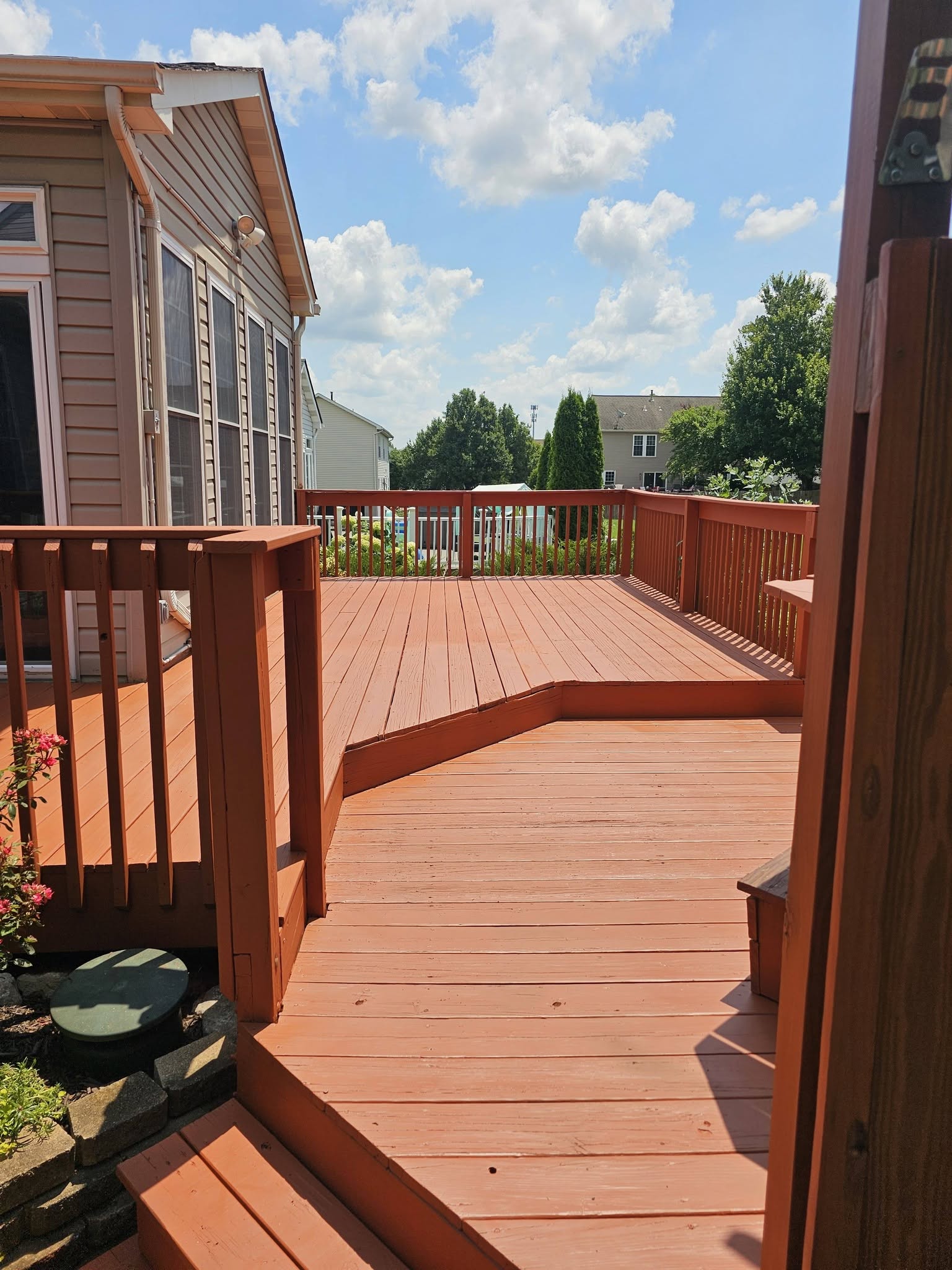 Red-stained wood deck with railing and steps in a suburban backyard